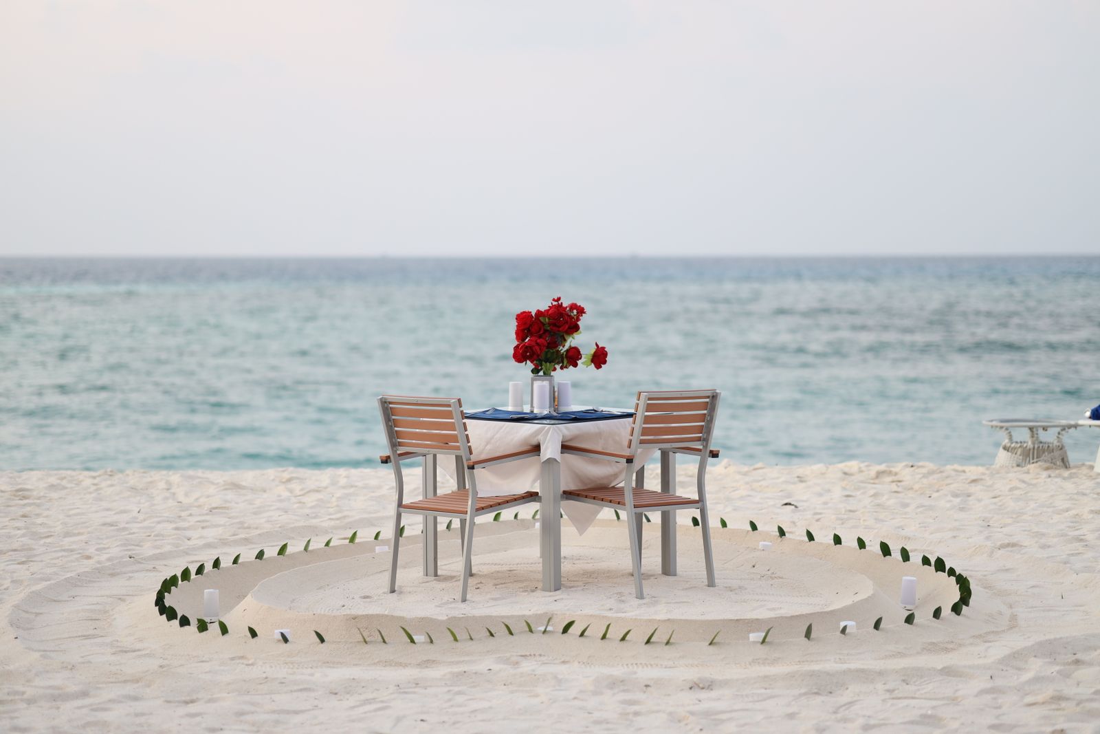A private candle-lit dinner table set on the sand by the ocean